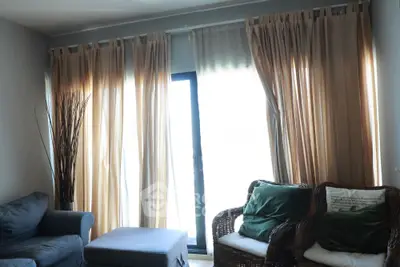 Cozy living room with natural light and elegant curtains, featuring comfortable seating and stylish decor.