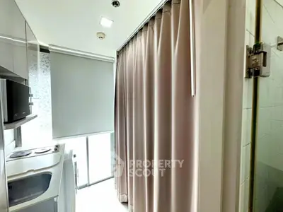 Compact kitchen with modern appliances and curtain divider in bright apartment