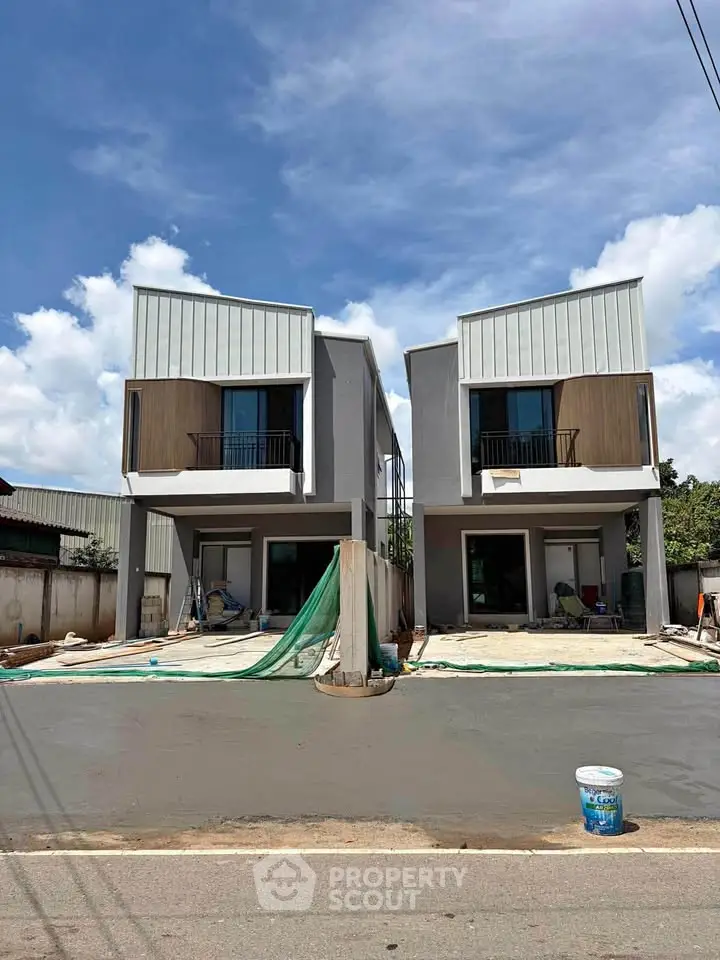 Modern twin townhouses with sleek design and spacious driveways under a clear blue sky.