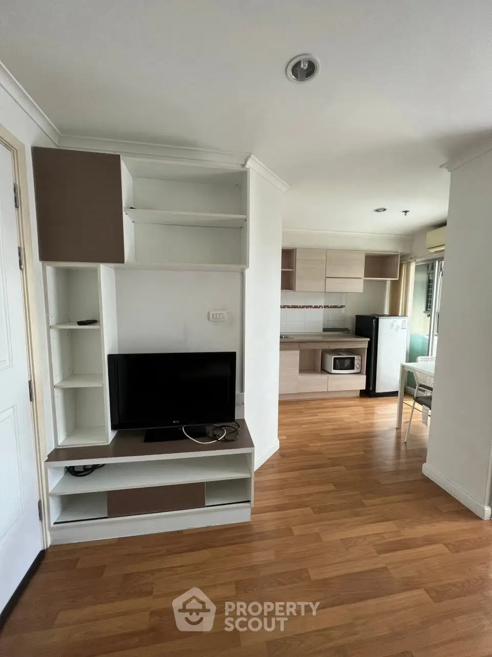 Modern apartment interior with open kitchen and living area, featuring wood flooring and built-in shelves.