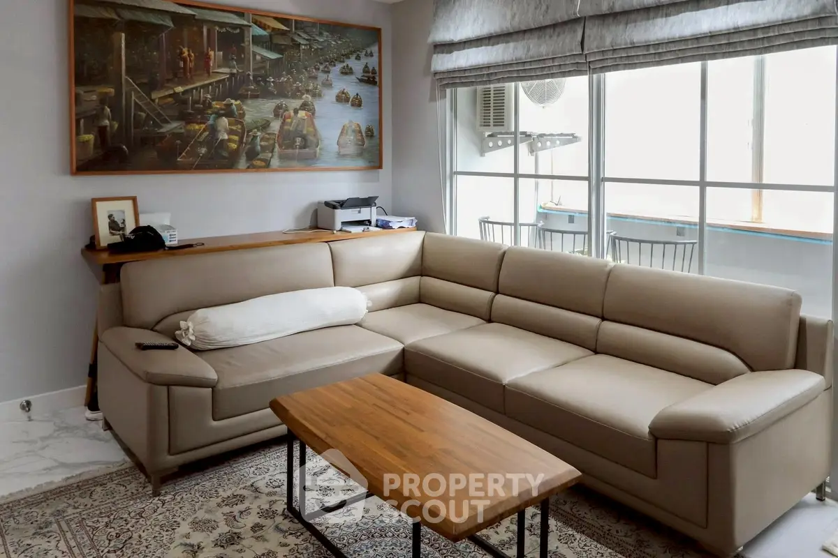 Spacious living room with modern beige sectional sofa and wooden coffee table, featuring large window for natural light.