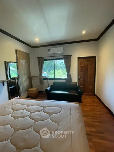Cozy bedroom with wooden flooring, large window, and air conditioning, perfect for relaxation.