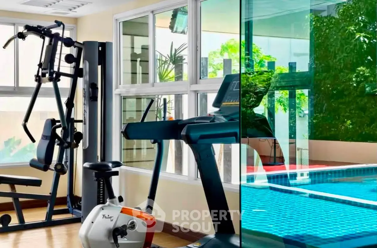 Modern gym with exercise equipment and pool view in luxury apartment complex.