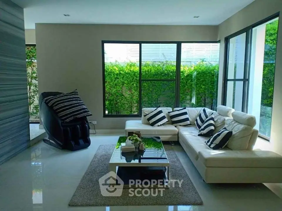 Modern living room with stylish furniture and large windows overlooking lush greenery.