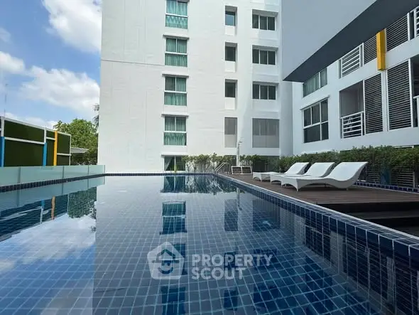 Modern apartment building with luxurious pool and stylish lounge chairs.