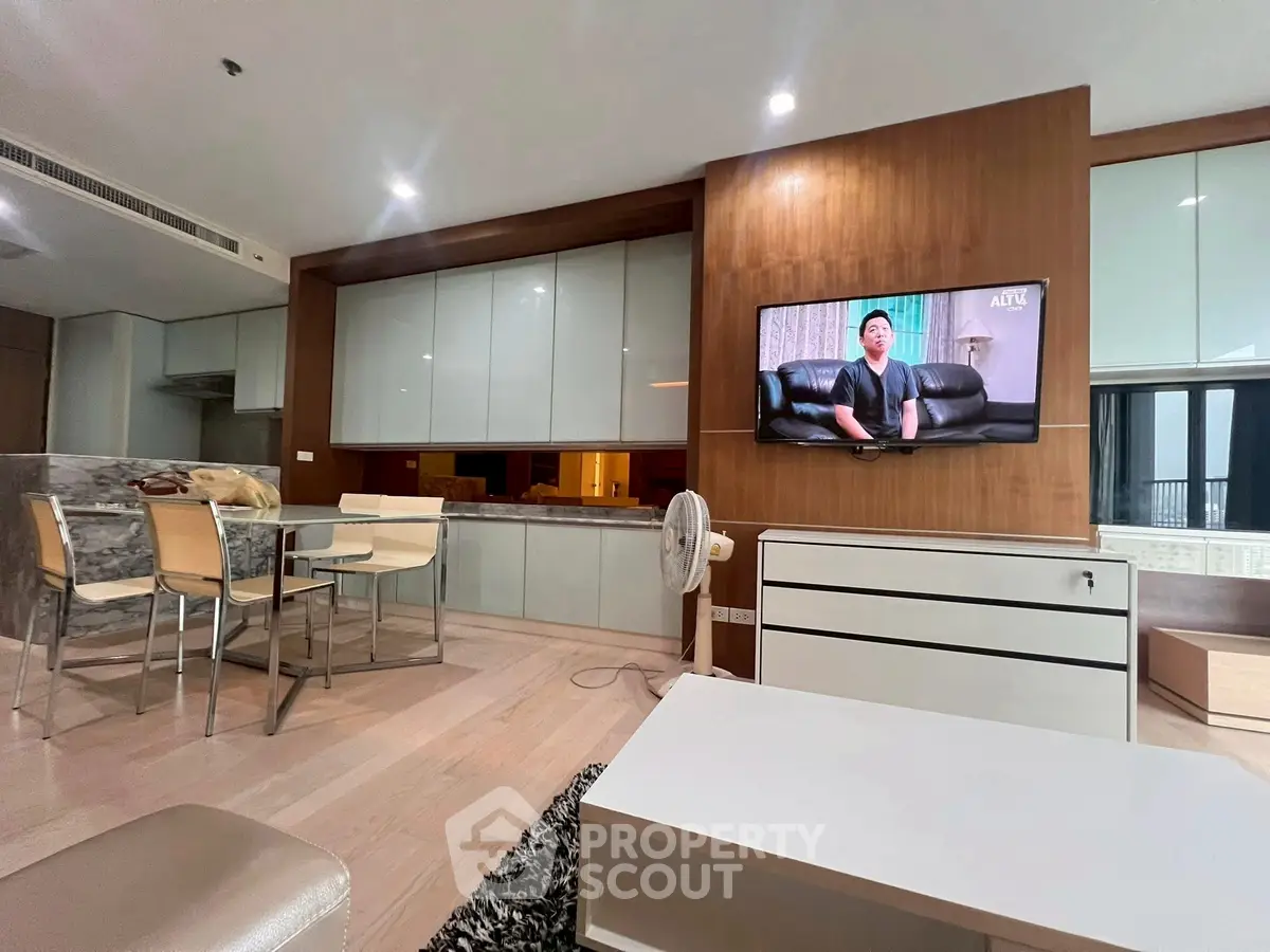 Modern living room with open kitchen, sleek furniture, and wall-mounted TV in a stylish apartment.