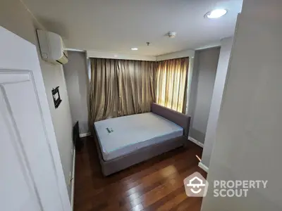 Cozy bedroom with wooden flooring and natural light from large windows.