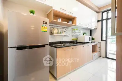Modern kitchen with sleek cabinets, stainless steel fridge, and large window for natural light.
