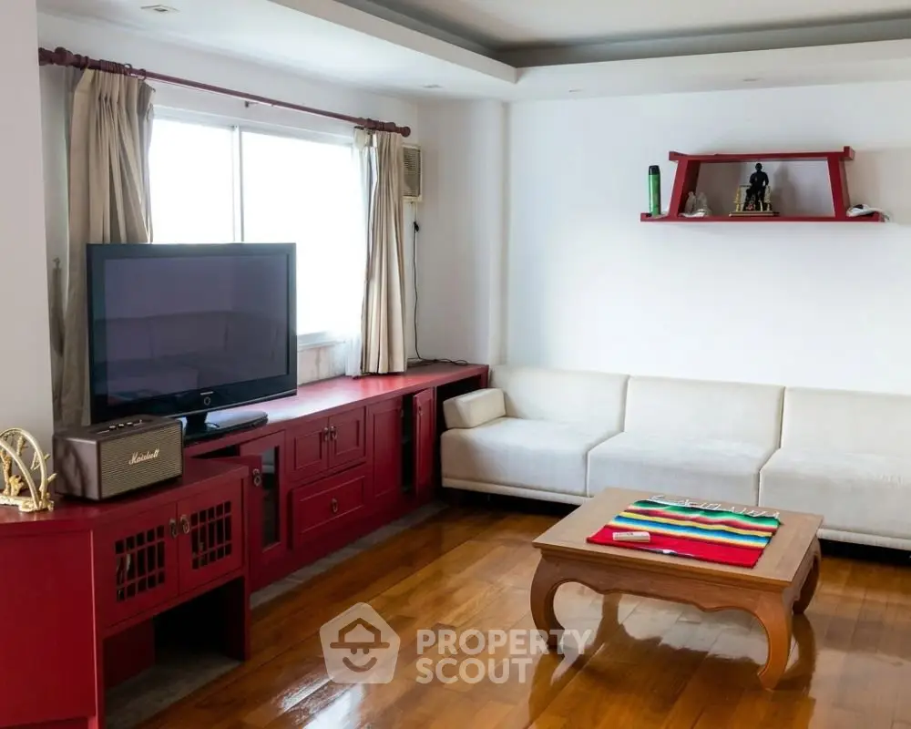 Spacious living room with modern decor and large TV, featuring wooden flooring and stylish red accents.