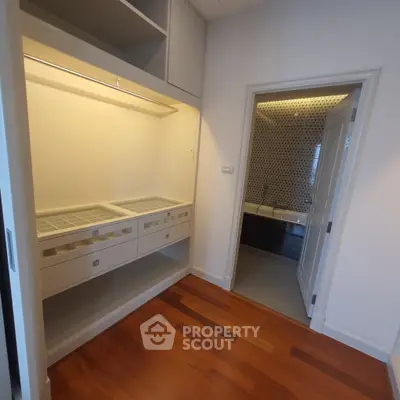 Spacious walk-in closet with elegant wooden flooring and view into modern bathroom.