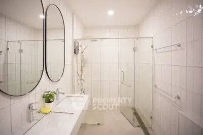 Modern bathroom with dual sinks and glass shower enclosure in sleek white tile design.