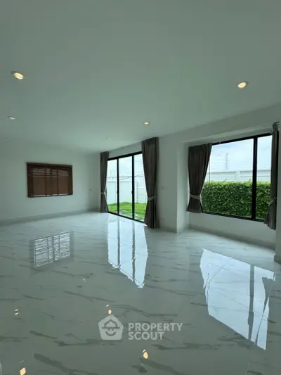 Spacious living room with large windows and garden view, featuring elegant marble flooring.