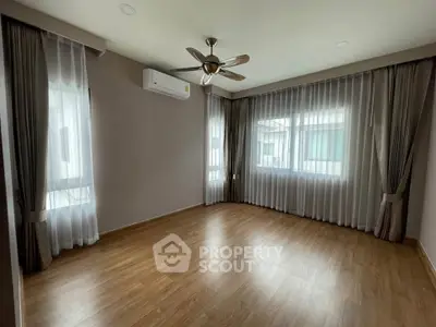 Spacious empty room with wooden flooring and large windows, perfect for customization.