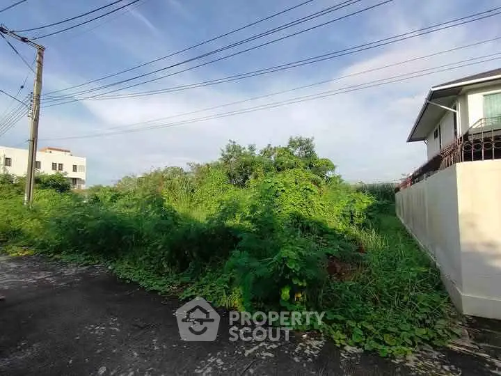 Vacant land with lush greenery and partial view of neighboring houses, ideal for development.