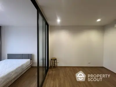 Modern bedroom with wooden flooring and glass partition in a minimalist apartment.