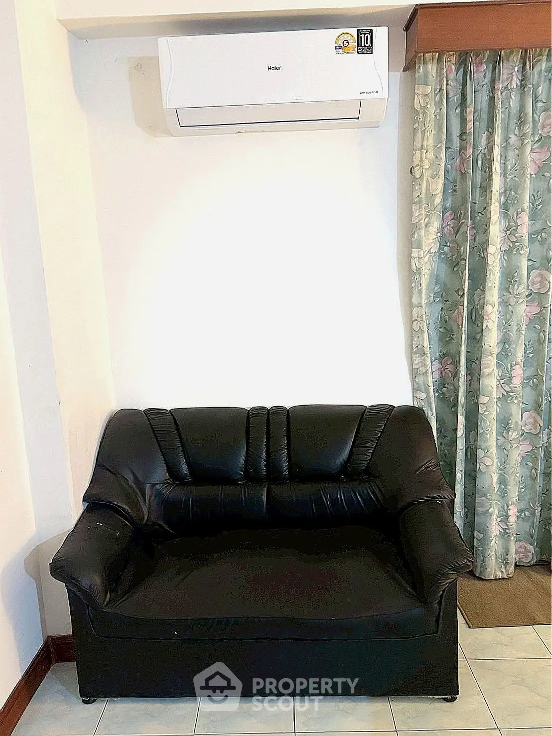 Cozy living room corner with black leather sofa and air conditioning unit.