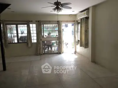 Spacious living room with large windows and ceiling fan, offering ample natural light.