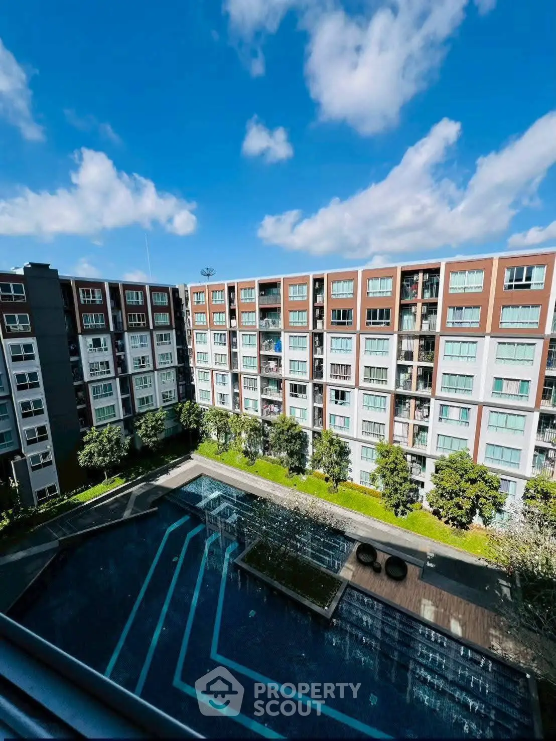 Stunning view of modern apartment complex with pool and lush greenery under blue skies.