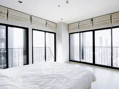 Bright modern bedroom with floor-to-ceiling windows and city view, featuring minimalist decor.