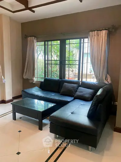 Modern living room with sleek black sectional sofa and glass coffee table, featuring large window view.