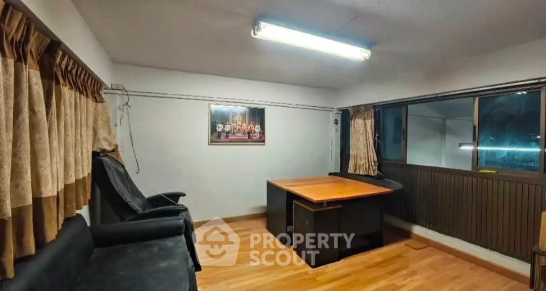 Spacious office room with wooden flooring and large window, ideal for professional workspace.