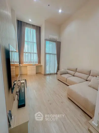 Spacious modern living room with high ceilings and large windows, featuring a cozy beige sofa and sleek entertainment setup.