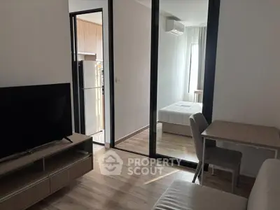Modern apartment interior with open living room and bedroom, featuring sleek furniture and natural light.