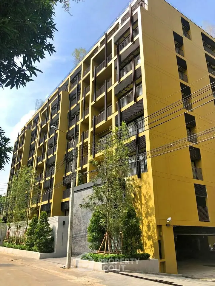 Modern yellow apartment building with lush greenery and clear blue sky.