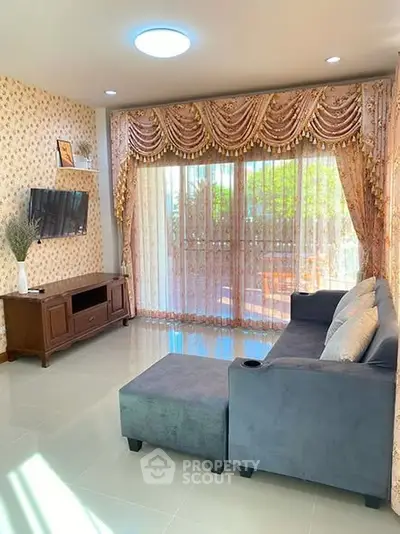 Elegant living room with plush sofa and ornate curtains, featuring a wall-mounted TV and natural light.