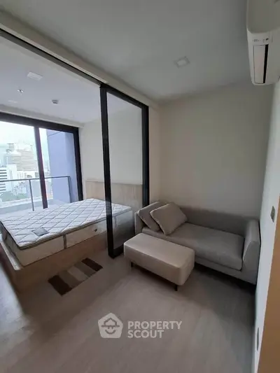 Modern bedroom with city view, featuring a cozy sofa and large windows for natural light.