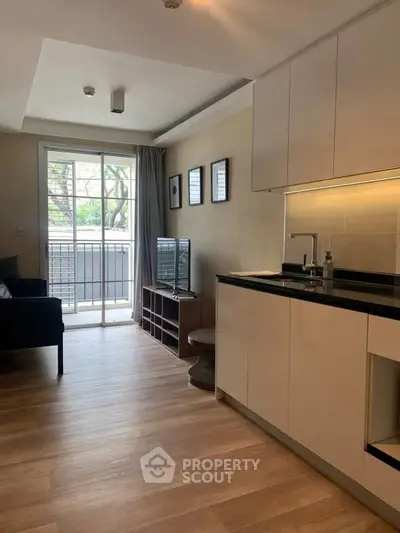 Modern living room with open kitchen and balcony view, featuring sleek cabinetry and cozy seating area.