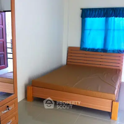 Cozy bedroom with minimalist wooden bed and matching side drawer, blue curtain accent, and tiled flooring, perfect for modern compact living.