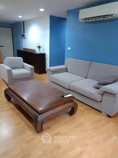Spacious living room with modern furniture and air conditioning, featuring a cozy sofa and armchair.