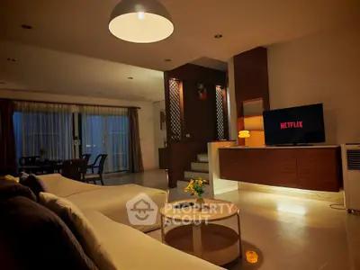 Spacious living room with modern decor and ambient lighting, featuring a cozy seating area and entertainment setup.