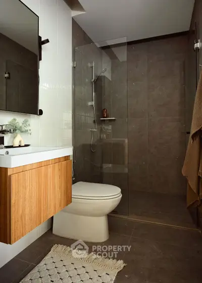 Modern bathroom with sleek design, featuring a glass shower and wooden vanity.