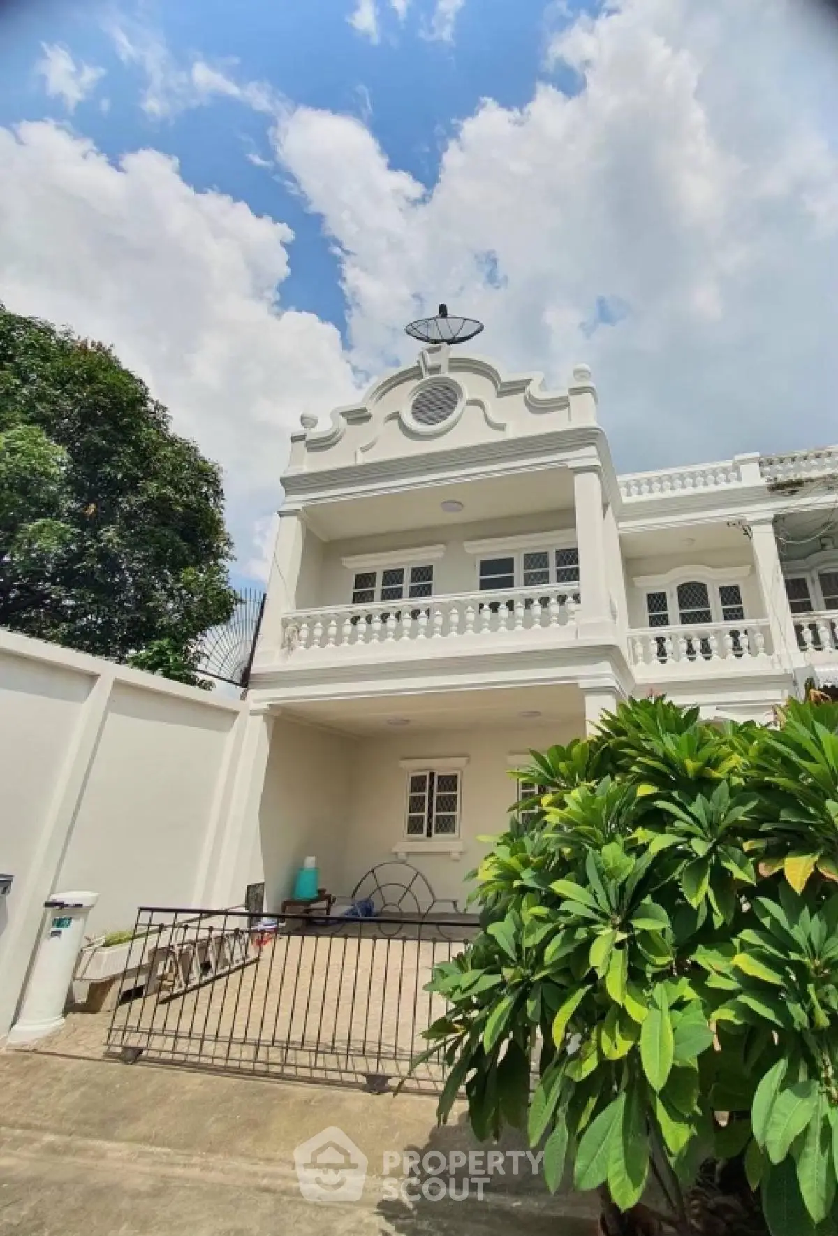 Charming colonial-style house with lush garden and spacious balcony under a bright blue sky.