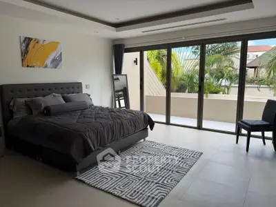 Spacious bedroom with modern decor and large windows opening to a private balcony with lush greenery.