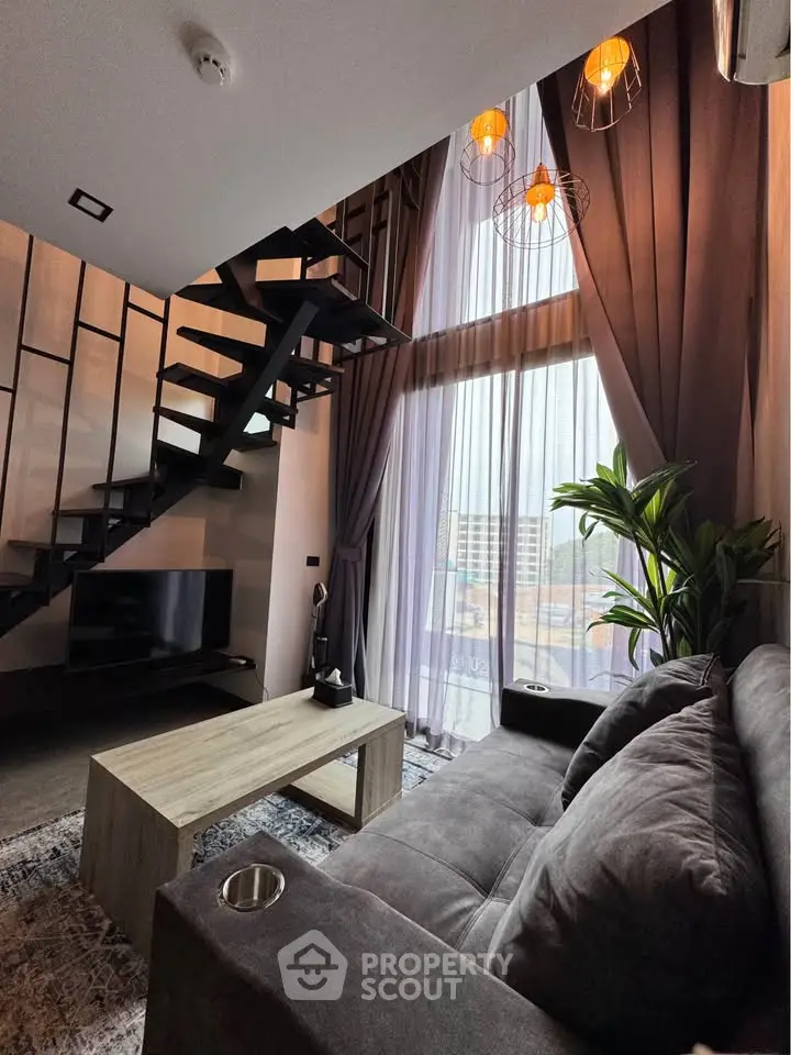 Modern living room with high ceiling, stylish staircase, and large window offering city views.