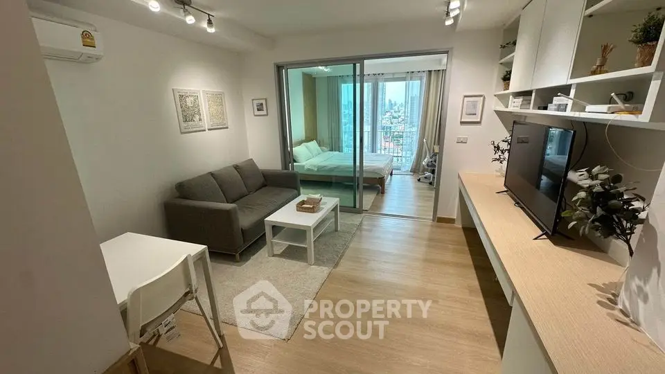 Modern studio apartment with open living area and city view, featuring sleek furniture and natural light.