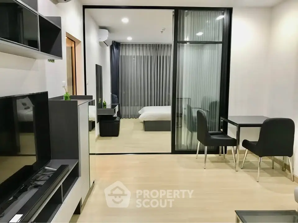 Modern open-plan living room with sleek furniture and glass partition leading to a cozy bedroom.