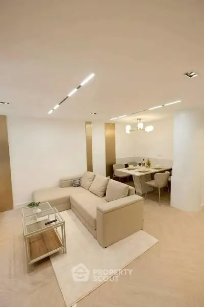 Modern living room with beige sofa and elegant dining area, featuring contemporary lighting and minimalist decor.