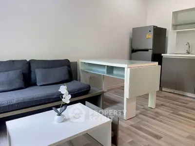 Modern living room with sleek furniture and stainless steel fridge in open layout.