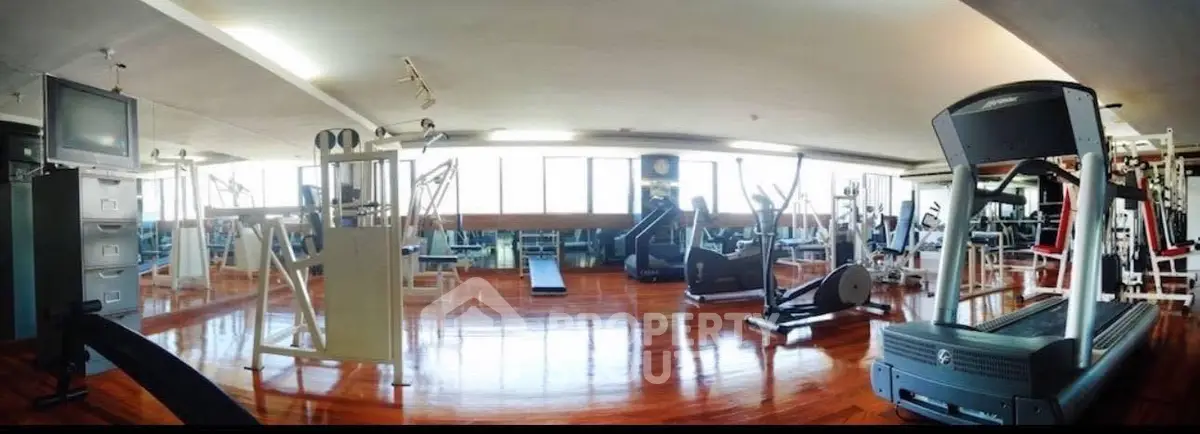 Spacious gym with modern equipment and wooden flooring in a well-lit area.