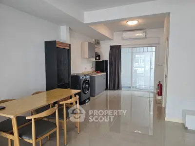 Modern open-plan living area with dining set and kitchen appliances, featuring sleek design and ample natural light.