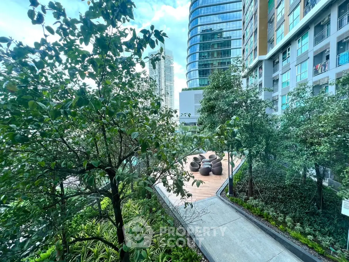 Modern urban garden with lush greenery and seating area in high-rise residential complex.