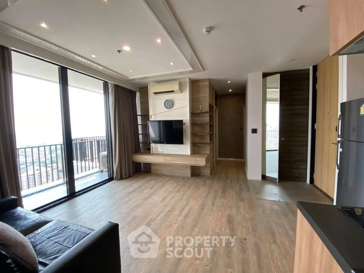 Spacious modern living room with large balcony and city view, featuring sleek wooden flooring and built-in entertainment unit.