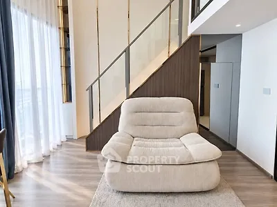 Modern living room with stylish staircase and cozy armchair, featuring elegant design and natural light.