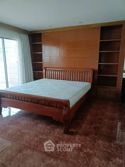 Spacious bedroom with elegant wooden bed and built-in shelves, featuring a large window for natural light.