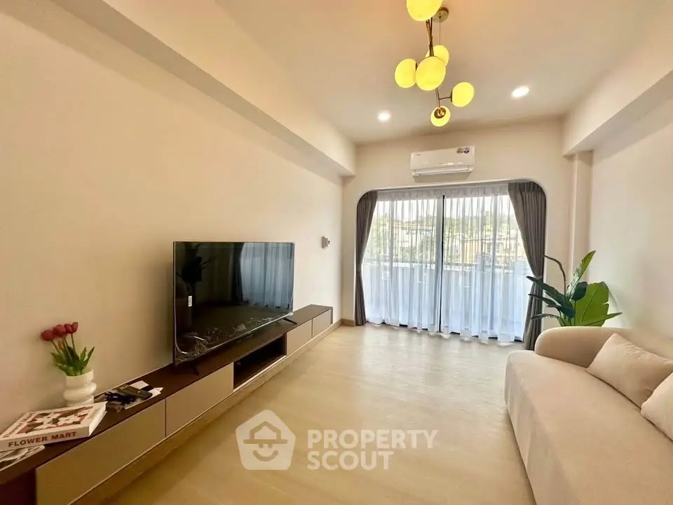 Modern living room with large TV, cozy sofa, and natural light from balcony.