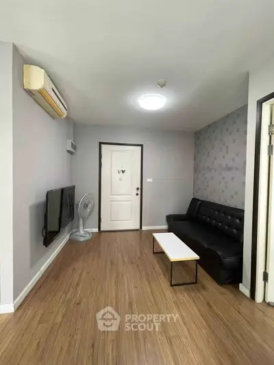 Modern living room with sleek black sofa, wall-mounted TV, and stylish decor in a cozy apartment.
